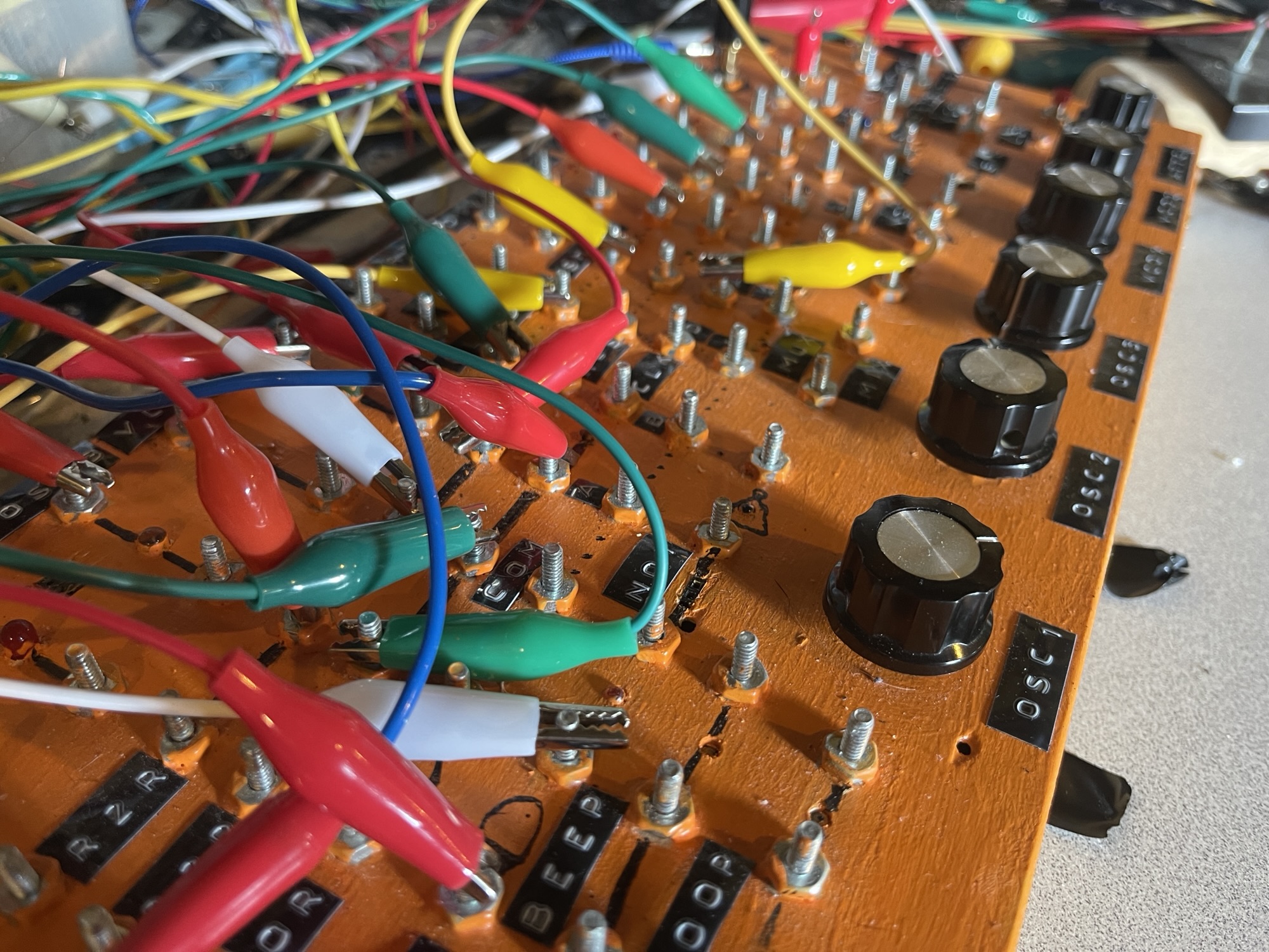 An orange synthesizer with knobs and tons of alligator clips