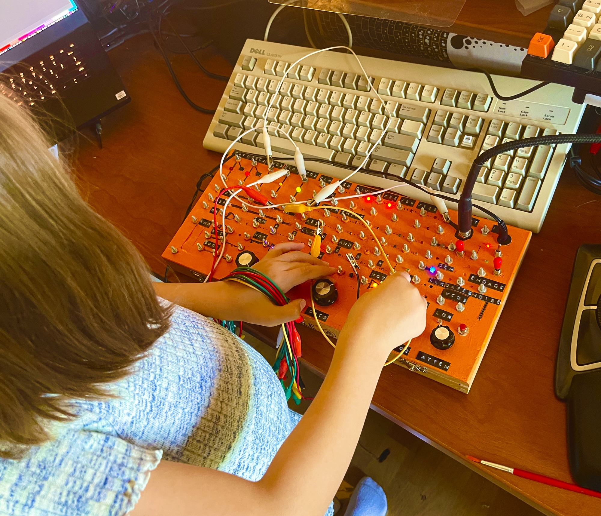 a kid playing an orange synthesizer with knobs and tons of alligator clips